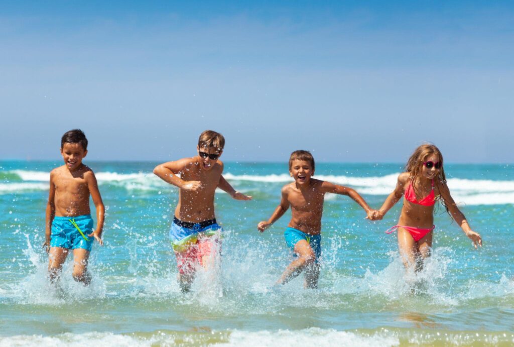 Four happy children running and splashing through the ocean waves on a sunny beach day